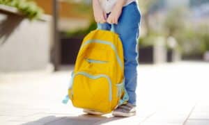 criança segurando mochila escolar amarela